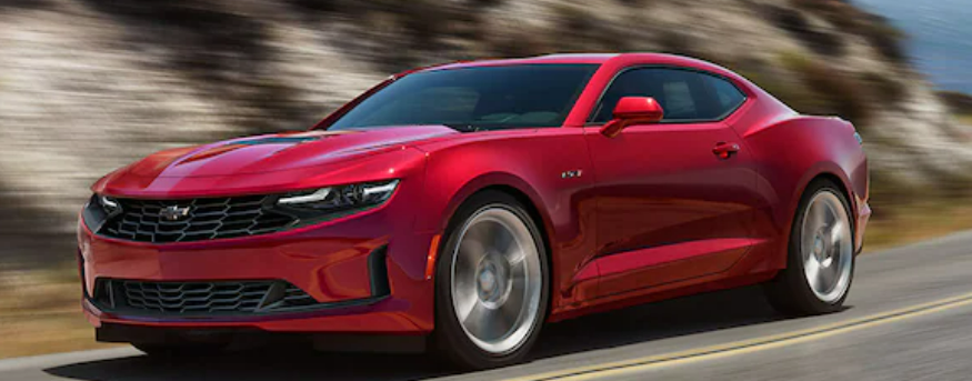 A dark red 2023 Chevrolet Camaro speeding down the road by a mountain