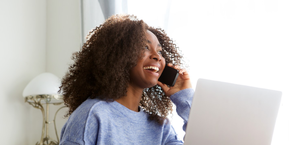 A woman searching the web on her laptop and also talking on her cellphone to a car dealer about buying a car