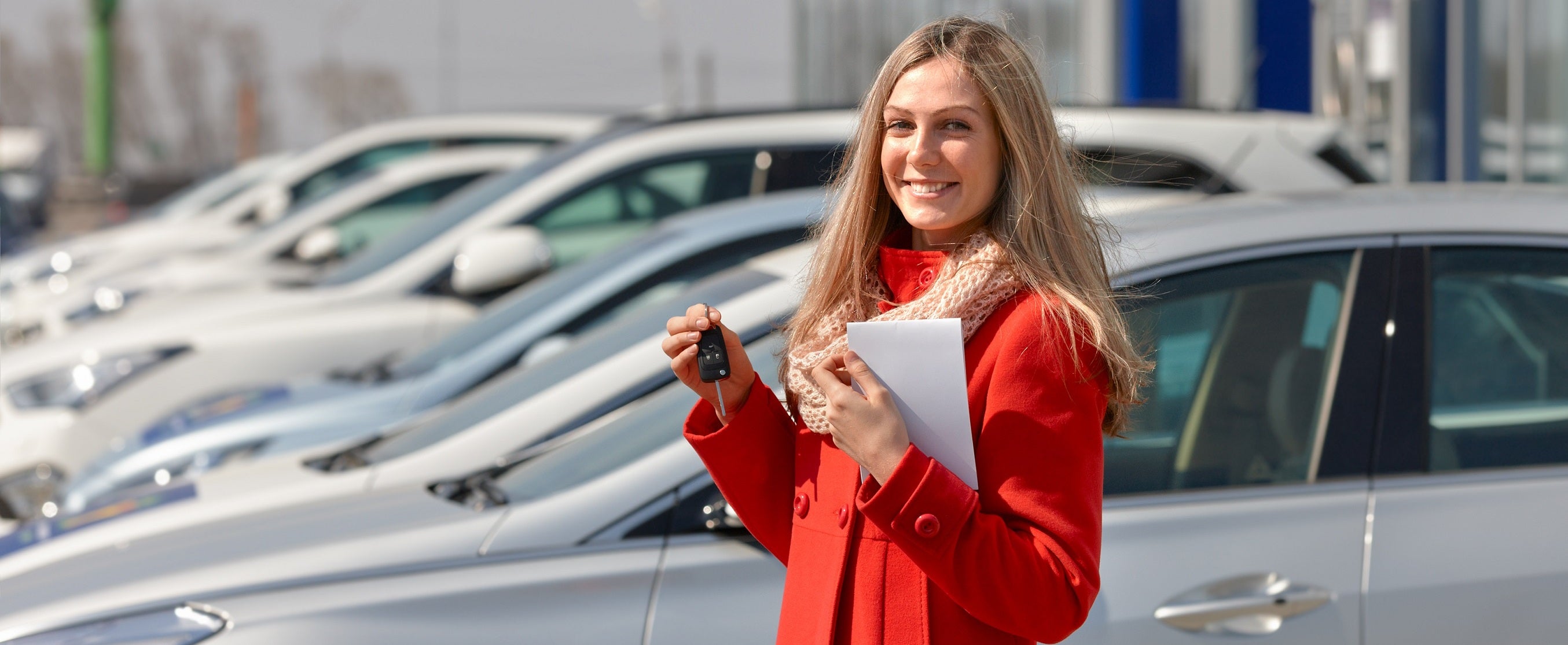 A woman in a red coat showing off the keys to her brand new car 